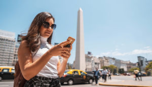 Turista brasileira mexendo no celular em frente ao Obelisco de Buenos Aires, onde o real ganhou poder de compra