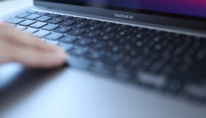 Close de mão tocando teclado de MacBook Air, da Apple, na cor cinza