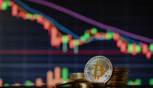 Conceito de Bitcoins nas cores dourada e prata, com gráfico caindo atrás, alusivo à venda da Tesla