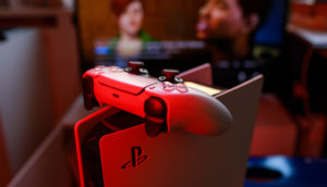 Detalhe de PlayStation 5 com controle em cima iluminados de vermelho e TV ao fundo, alusivo à subida de preço realizada pela Sony