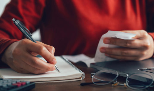 Close de pessoa de suéter vermelho fazendo contas, alusivo ao endividamento das famílias