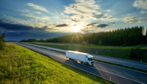 Caminhão branco rodando em estrada com árvores ao fundo e pôr do sol, alusivo às ações da Vamos, que entraram para a carteira ESG