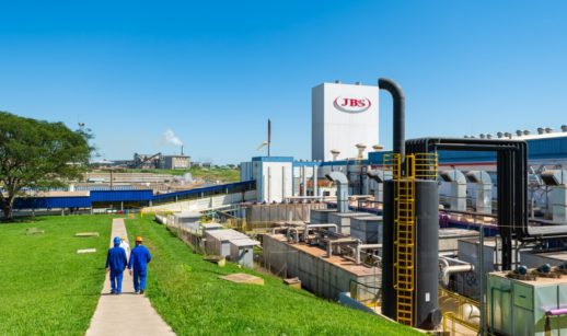 Fábrica da JBS, que teve lucro, com dois funcionários caminhando em gramado