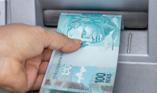 Mão puxando duas notas de 100 reais, alusivo ao saque do golpe do FGTS