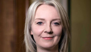 Liz Truss, sorrindo de boca fechada, olhando pra frente,