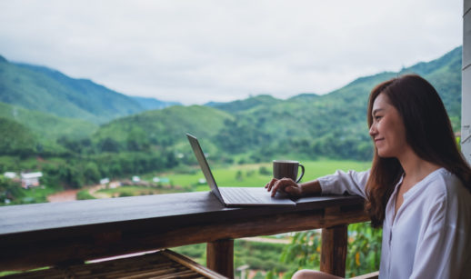Jovem mulher com computador em varanda nas montanhas, alusivo às finanças sustentáveis
