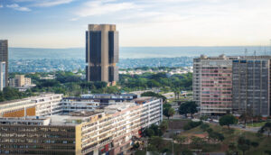 Vista panorâmica de Brasília com destaque para o edifício-sede do Banco Central do Brasil, cercado por prédios comerciais e áreas verdes, sob céu parcialmente nublado