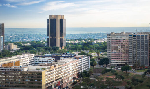 Vista panorâmica de Brasília com destaque para o edifício-sede do Banco Central do Brasil, cercado por prédios comerciais e áreas verdes, sob céu parcialmente nublado