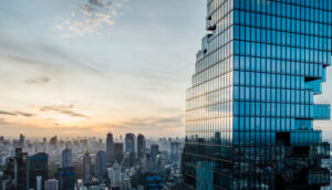 Prédio comercial moderno com fachada espelhada em destaque, refletindo o horizonte urbano ao pôr do sol, com diversos edifícios ao fundo