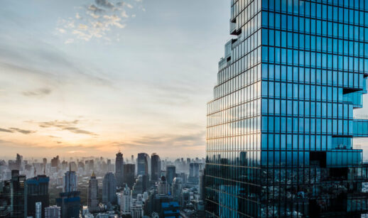 Prédio comercial moderno com fachada espelhada em destaque, refletindo o horizonte urbano ao pôr do sol, com diversos edifícios ao fundo
